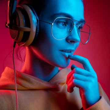 open-back headphones woman with glasses and hoodie wearing headphones red background